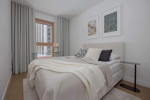 Ein modernes Schlafzimmer mit einem Bett, einem Nachttisch, einem Fenster mit Vorhängen und zwei gerahmten Kunstwerken an der Wand.