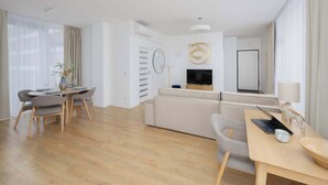 A modern living room with a sofa, dining table, and chairs. There is a TV, a lamp, and a small statue on the table. - Stylish Apartment | Balcony, Air Conditioning, Workspace (Warszawa)