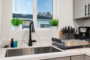 Moderni keittiö, jossa on ruostumattomasta teräksestä valmistettu allas, musta hana ja veitsiteline.