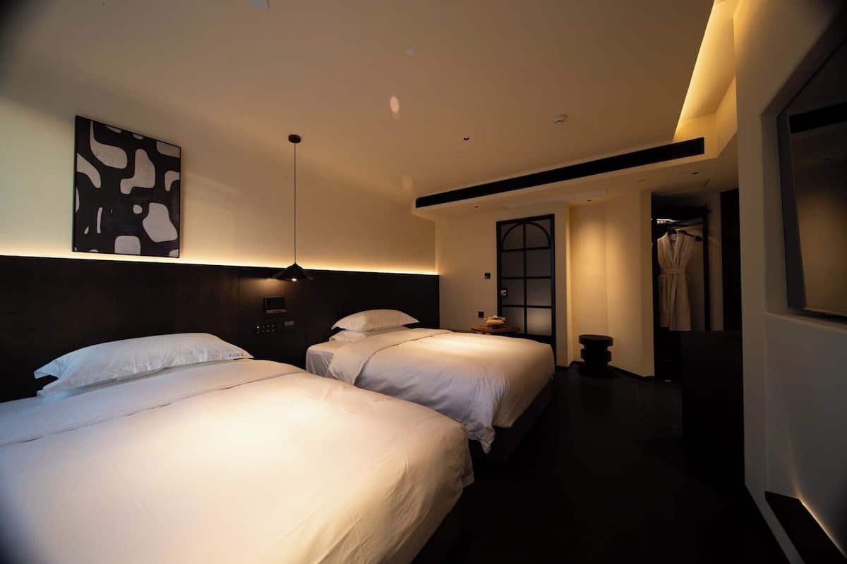 A hotel room with two beds, a large abstract painting on the wall, and a robe hanging by the door.