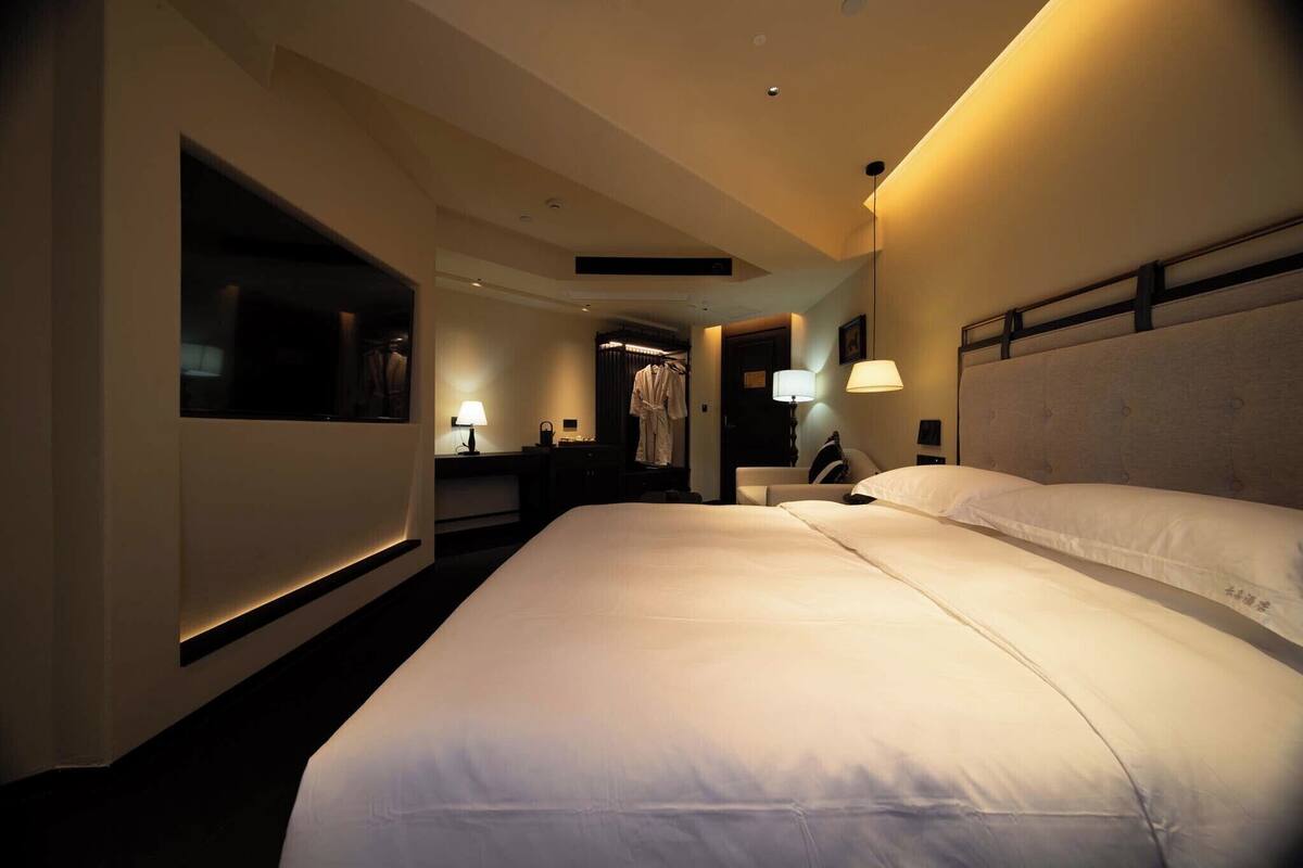 A hotel room with a large bed, bedside lamps, a wardrobe, and a mirror.