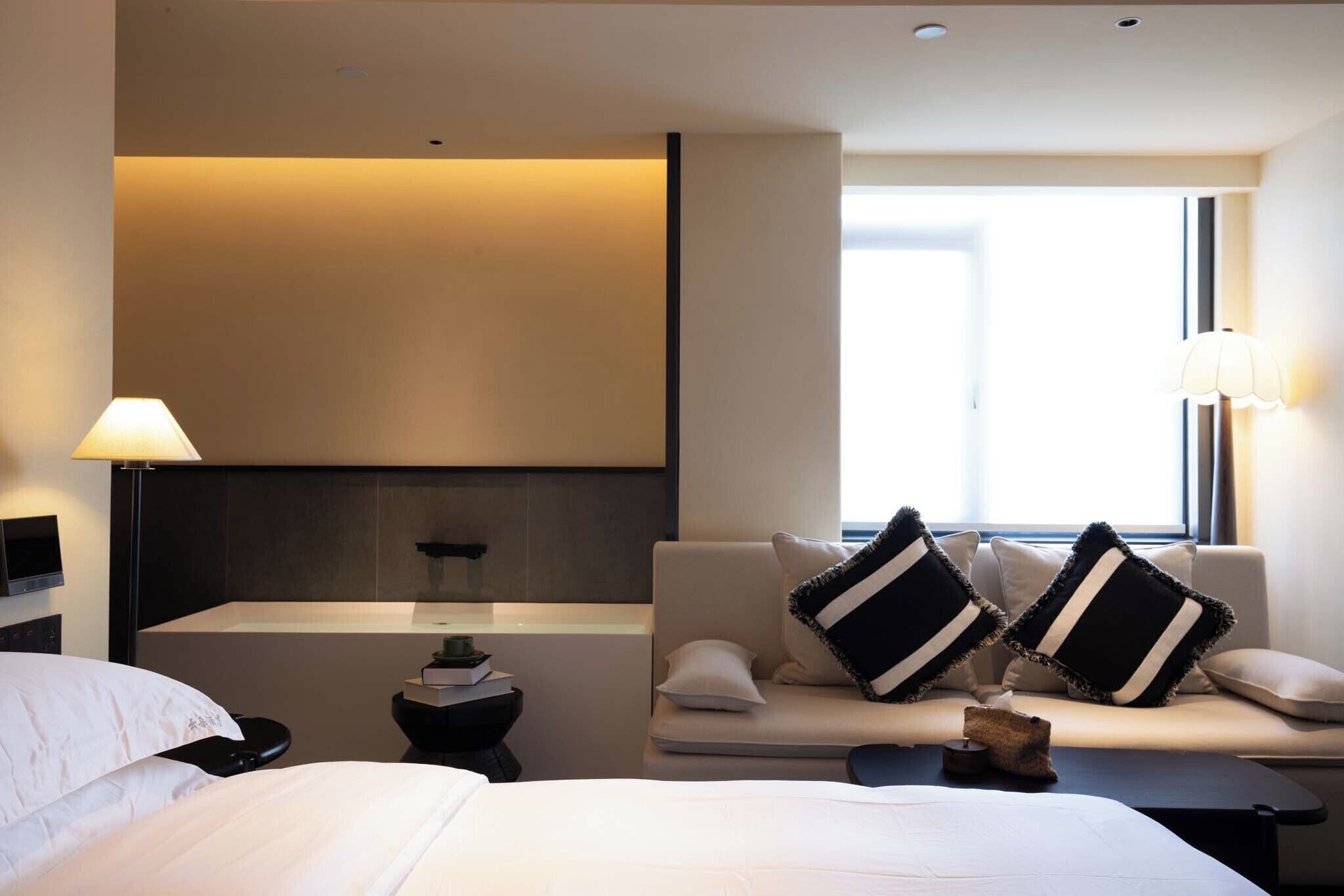 A modern hotel room with a bed, a sofa, a small table, and a nightstand.