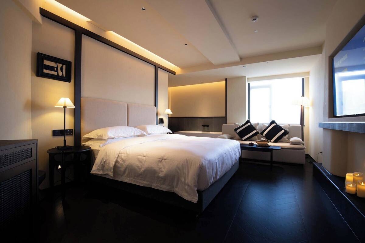 A modern hotel room with a large bed, bedside tables, a sofa, and a TV.