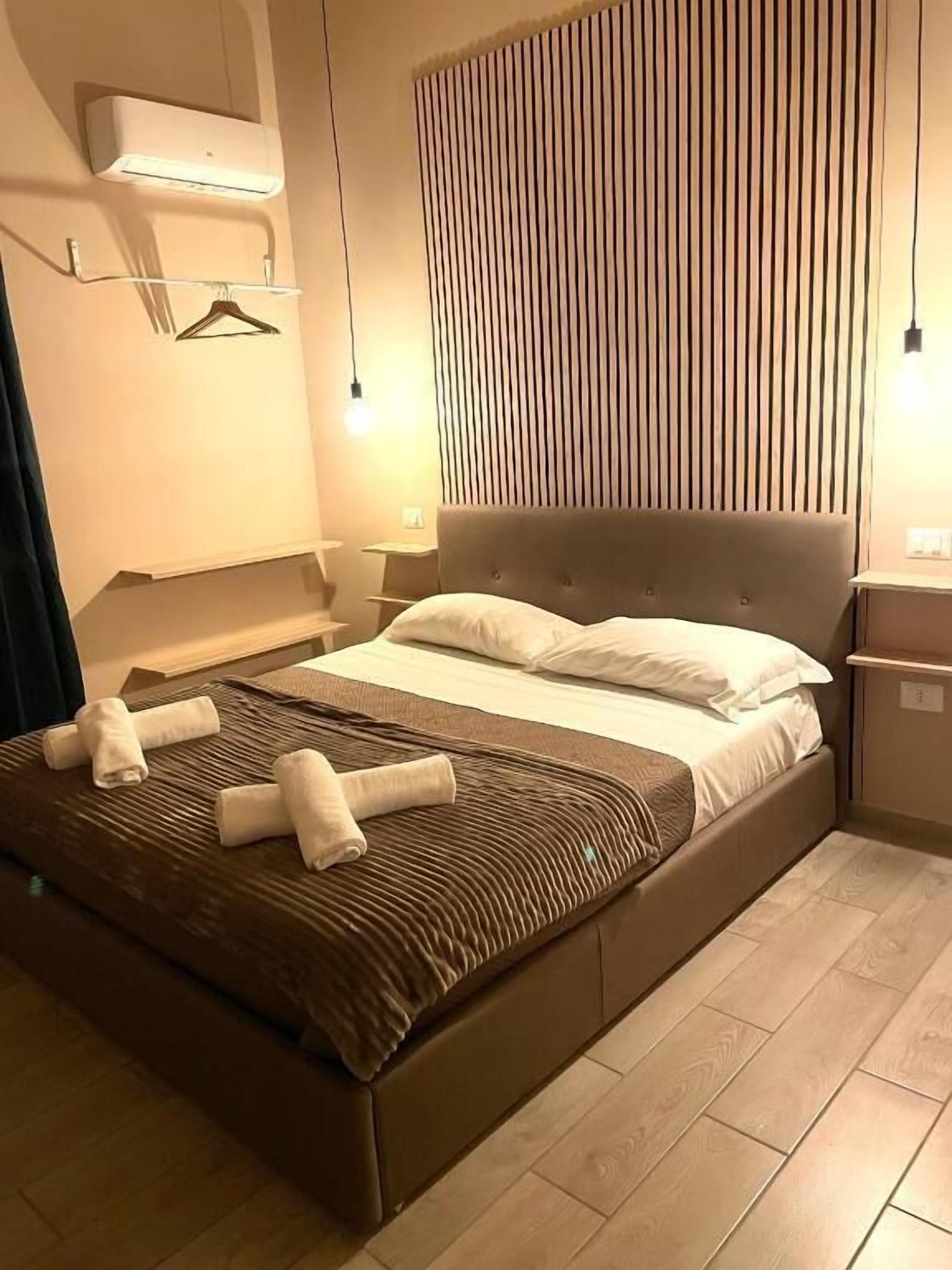 A modern bedroom with a large bed, bedside tables, a wall-mounted air conditioner, and a vertical slat design on the wall.