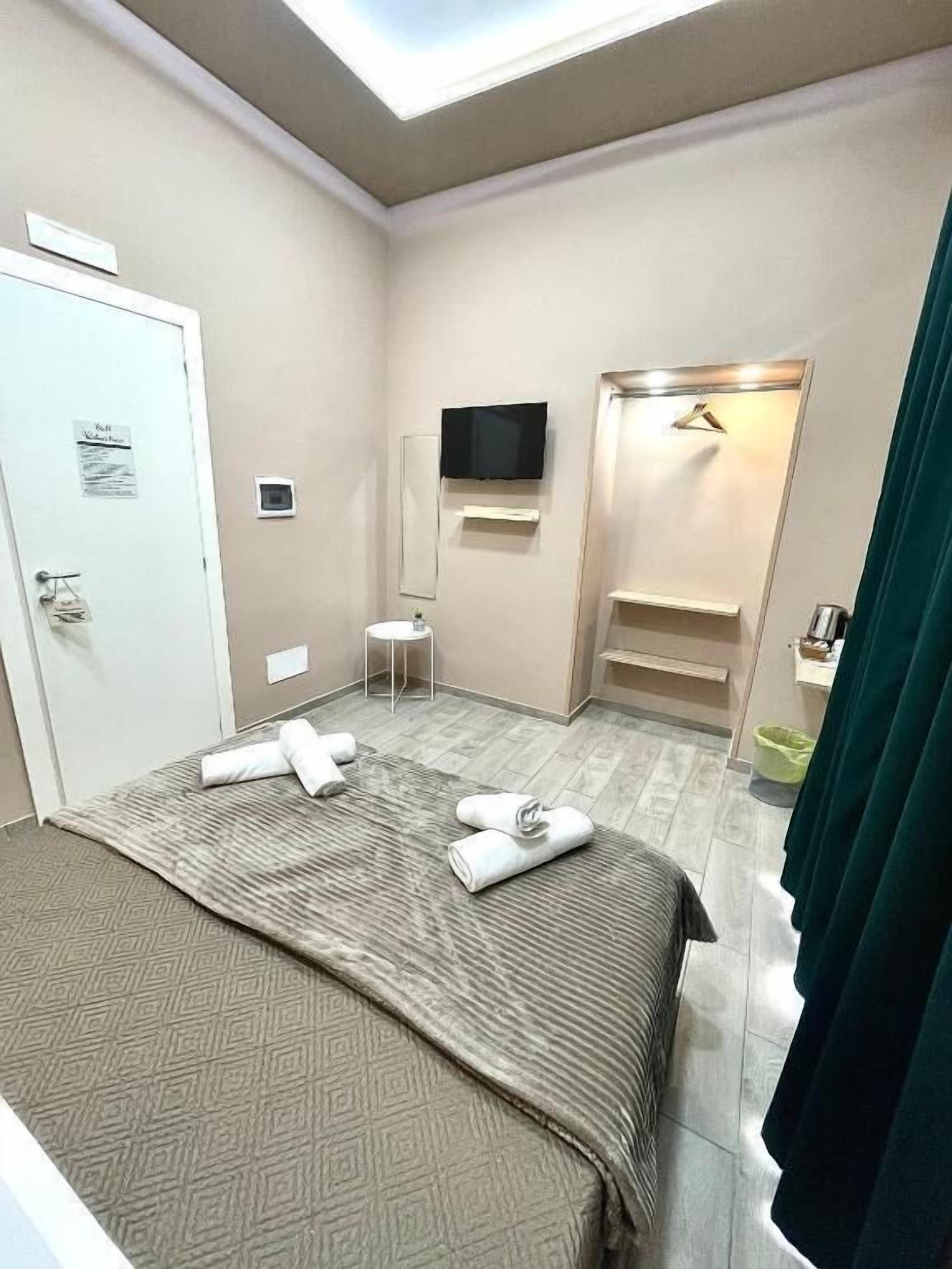 A hotel room with a bed, a TV mounted on the wall, a small table, and a shower area.