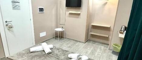 A hotel room with a bed, a TV mounted on the wall, a small table, and a shower area.