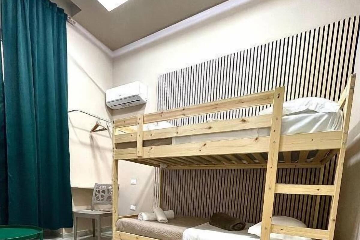 Une chambre avec un lit superposé, une lucarne, une table et une chaise.
