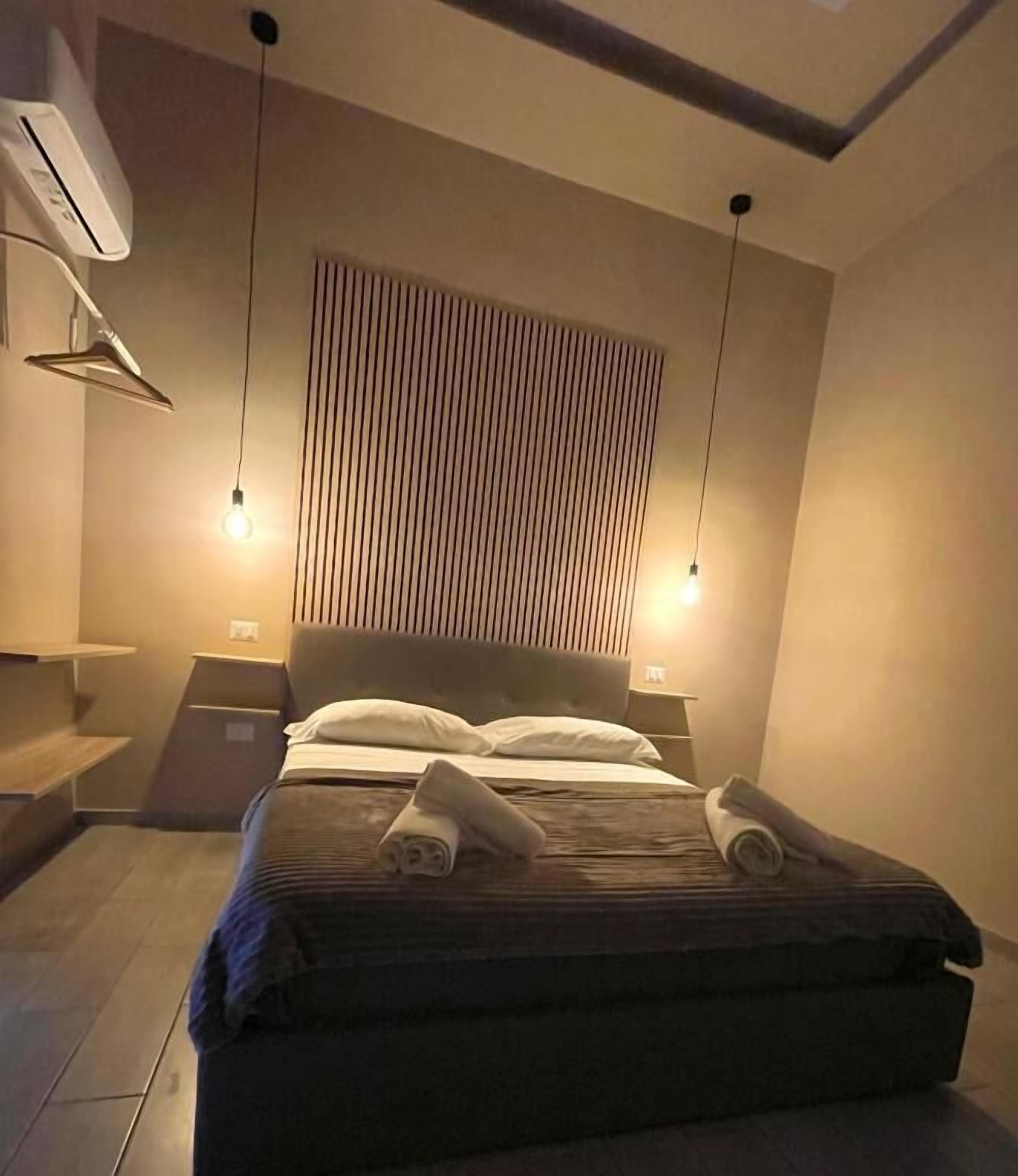 A modern bedroom with a bed, bedside tables, and a wall-mounted light fixture.