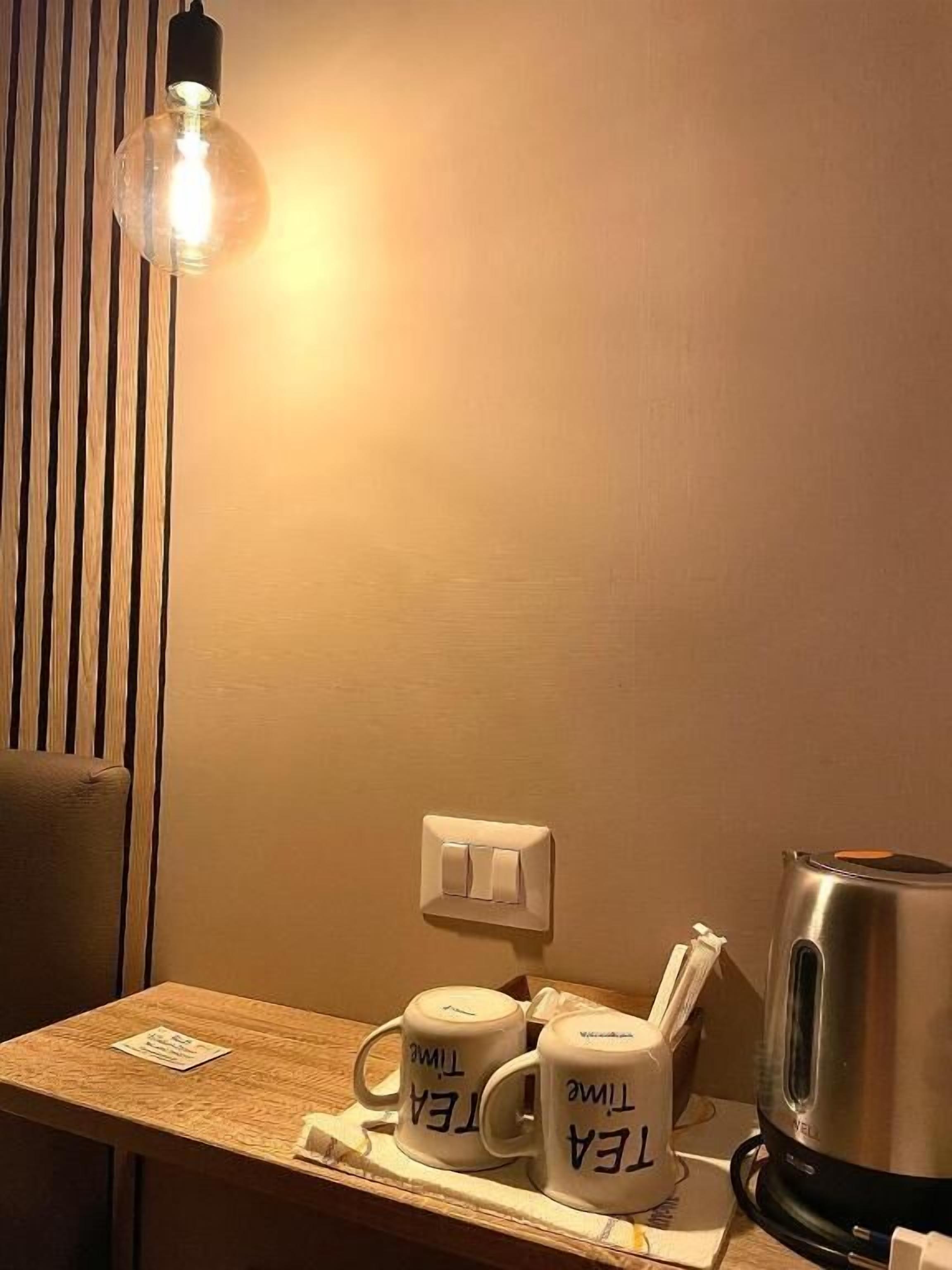 Une pièce chaleureuse avec un mur lambrissé en bois, une ampoule suspendue, une machine à café et deux tasses sur lesquelles est inscrit « HEURE DU THÉ ».