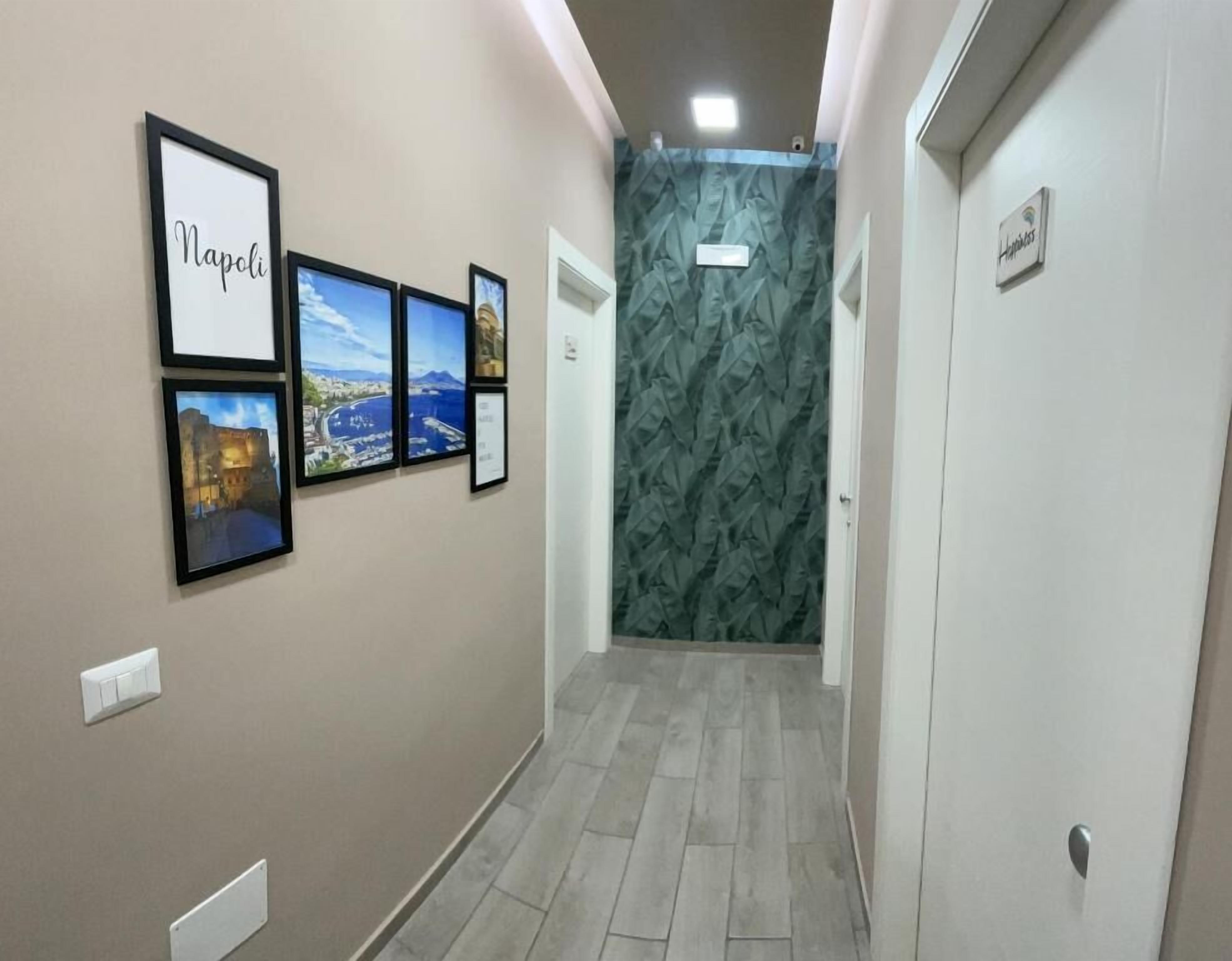 A hallway with framed pictures on the wall, a patterned wallpaper, and a door with a sign.