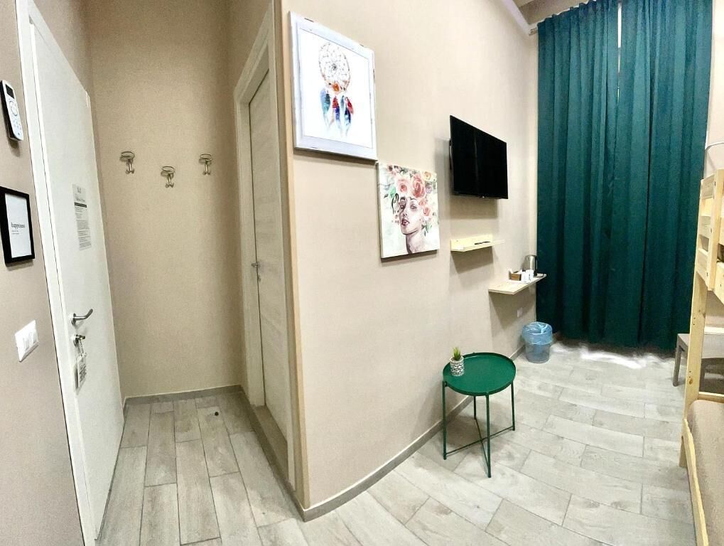 A room with a bed, a television mounted on the wall, a small table, and a green chair.