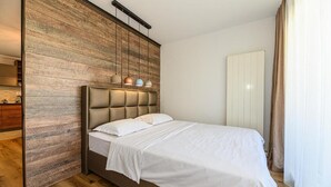 A bedroom with a wooden accent wall, a tufted headboard, a white bedspread, and pendant lighting.