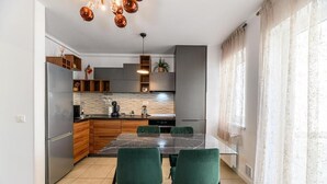 A modern kitchen with a marble island, wooden cabinets, and green chairs.
