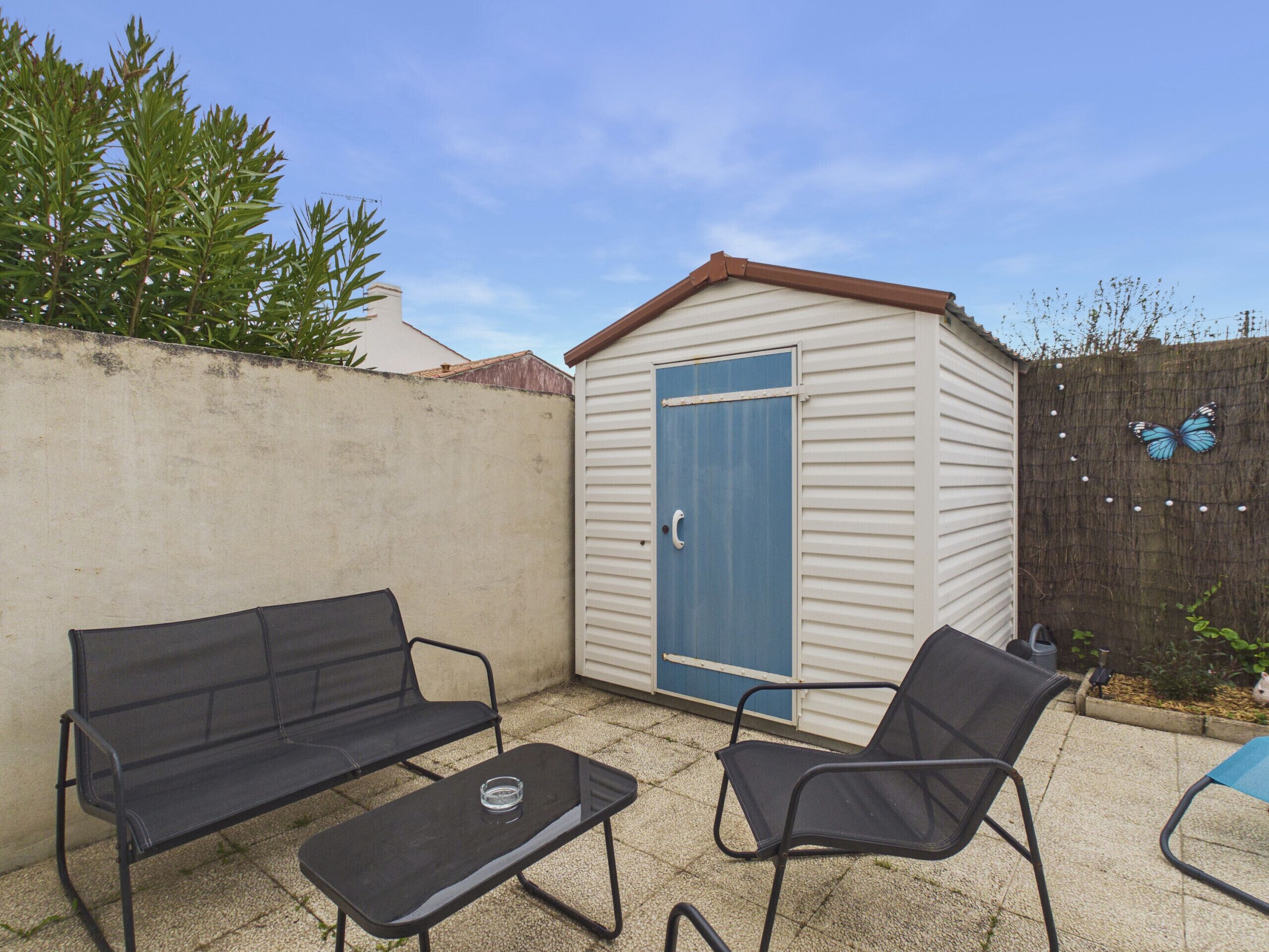 A small shed with a blue door, a black metal bench, a metal table, and a blue chair in a backyard with a concrete floor.