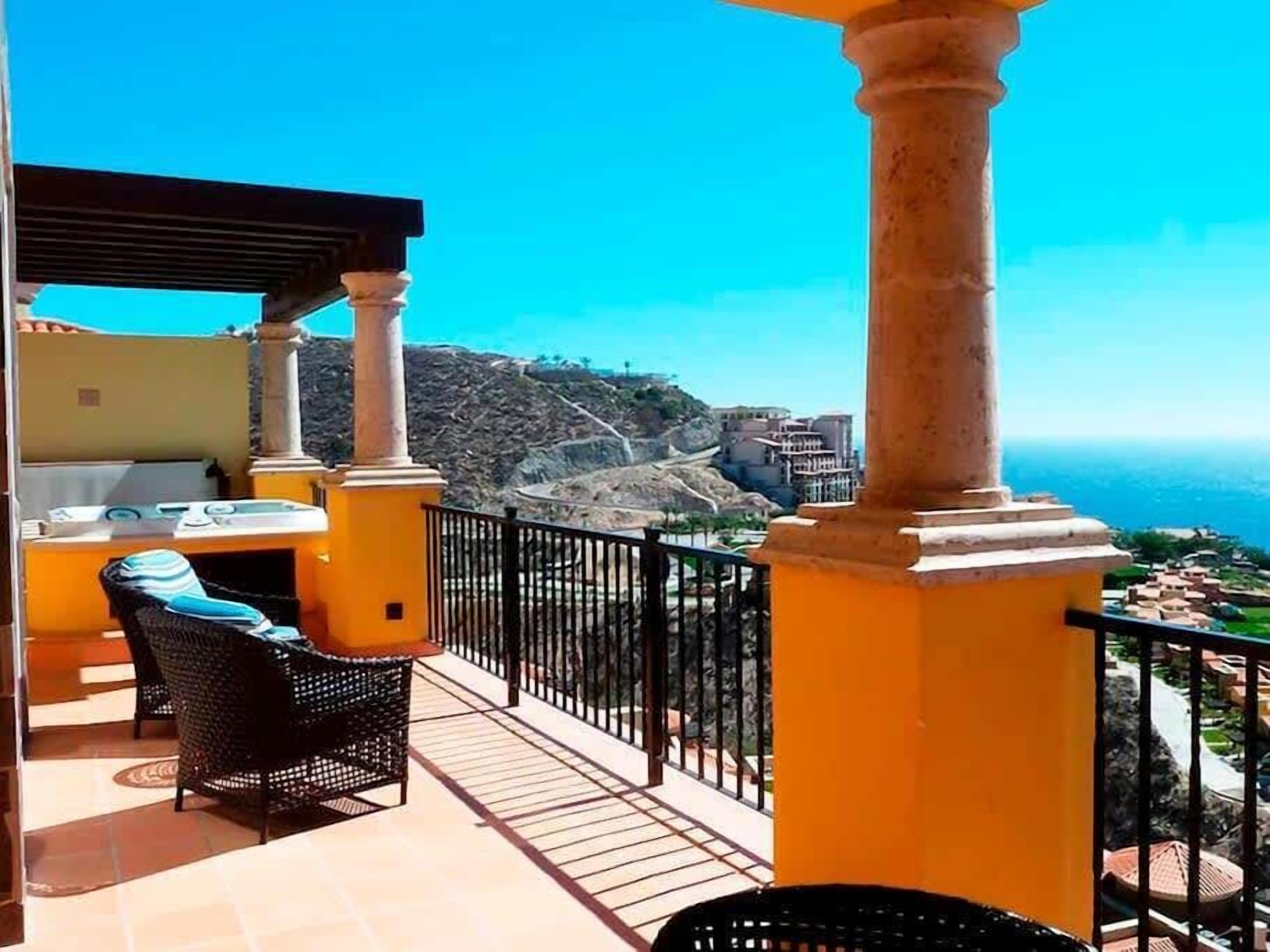 A balcony with a view of the sea, featuring a table and chairs, and a pergola structure.