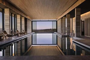 A modern indoor swimming pool with a clear view of the landscape, wooden ceiling, and lounge chairs along the poolside. - Fantastic 4BR Residence with Ocean View (Tsada)