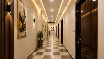 A hotel hallway with checkered flooring, wall-mounted artwork, and doors leading to rooms.