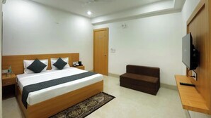 Une chambre d’hôtel avec un lit en bois, une télévision, un petit canapé et une porte.