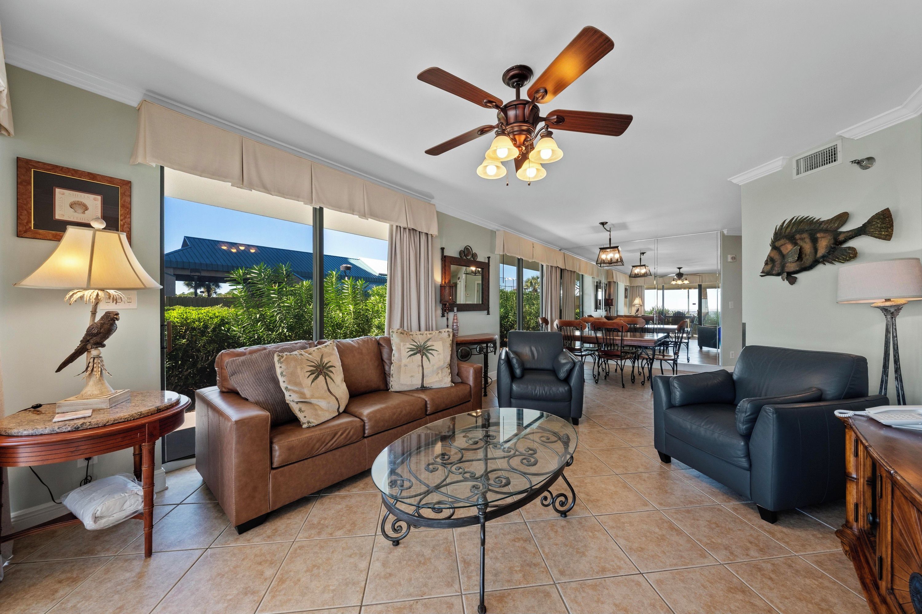A spacious living area with a ceiling fan, a glass coffee table, leather sofas, and a dining area with chairs.