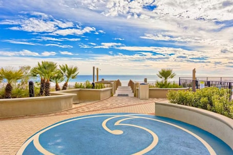 A pathway leading to a beach with palm trees and a blue circular design on the ground.