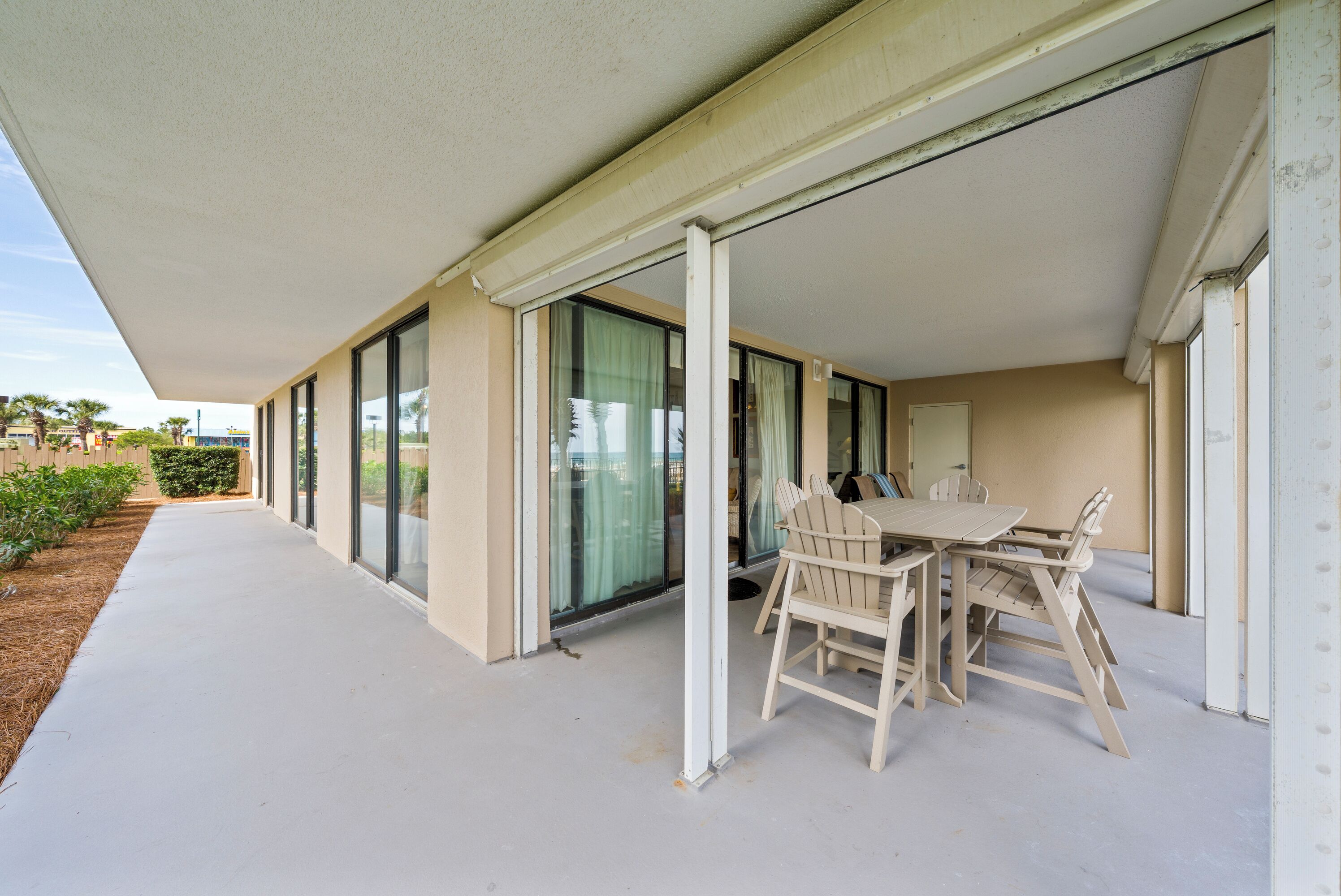 A covered outdoor area with a table and chairs, large sliding glass doors, and a concrete floor.