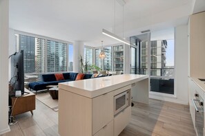 A modern apartment with a kitchen, living area, and large windows offering city views. - King Bed | Mins to Stampede | Cgy Twr View | UG Pk (Calgary)
