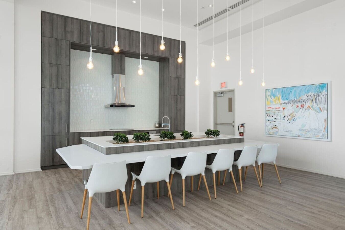 A modern kitchen with a central island, white chairs, pendant lighting, and a large painting on the wall.