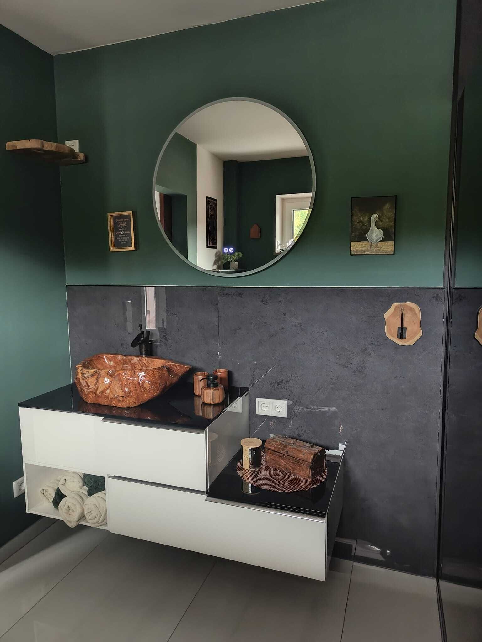 Une salle de bain moderne avec un grand miroir ovale, un plan de travail noir et un meuble blanc.