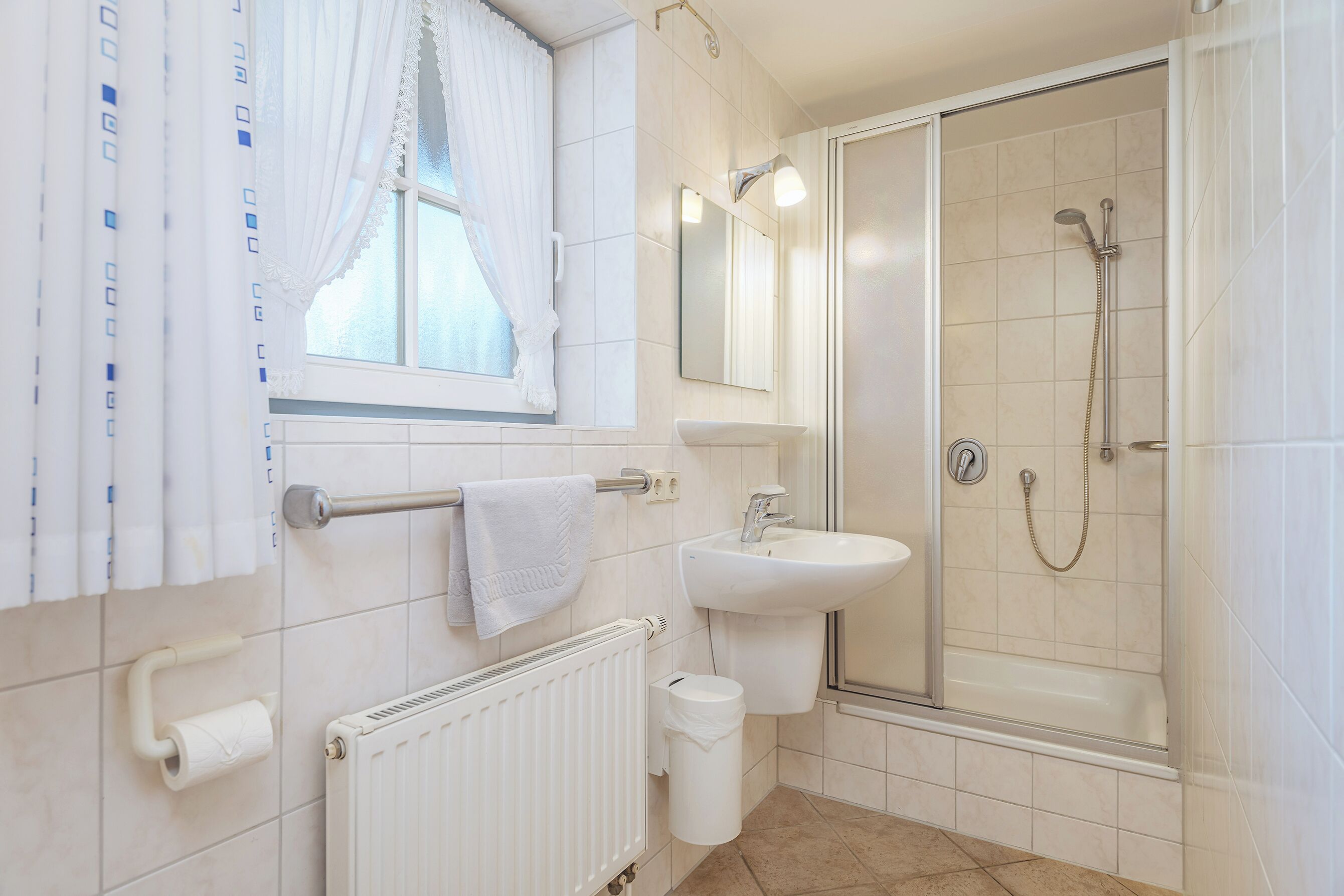 Une salle de bain équipée d’une douche, d’un lavabo, de toilettes et d’une fenêtre avec des rideaux.