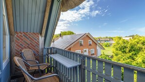 Ein Balkon mit Korbstühlen, einem Tisch und Blick auf ein rotes Haus und Grünflächen.