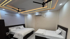 Une chambre avec deux lits, un ventilateur de plafond, des spots encastrés et un appareil de climatisation.