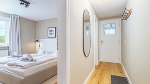 A bedroom with a bed, a bedside table, a mirror, and a window with curtains. - Modern living under thatch - your stylish Bodden break for two (Born a. Darß)