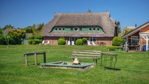 A thatched-roof building with a green facade, a grassy lawn, and outdoor seating. - Modern living under thatch - your stylish Bodden break for two (Born a. Darß)