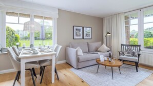 A living room with a sofa, a dining table set, a coffee table, and a chair with a zebra print cushion. - Modern living under thatch - your stylish Bodden break for two (Born a. Darß)