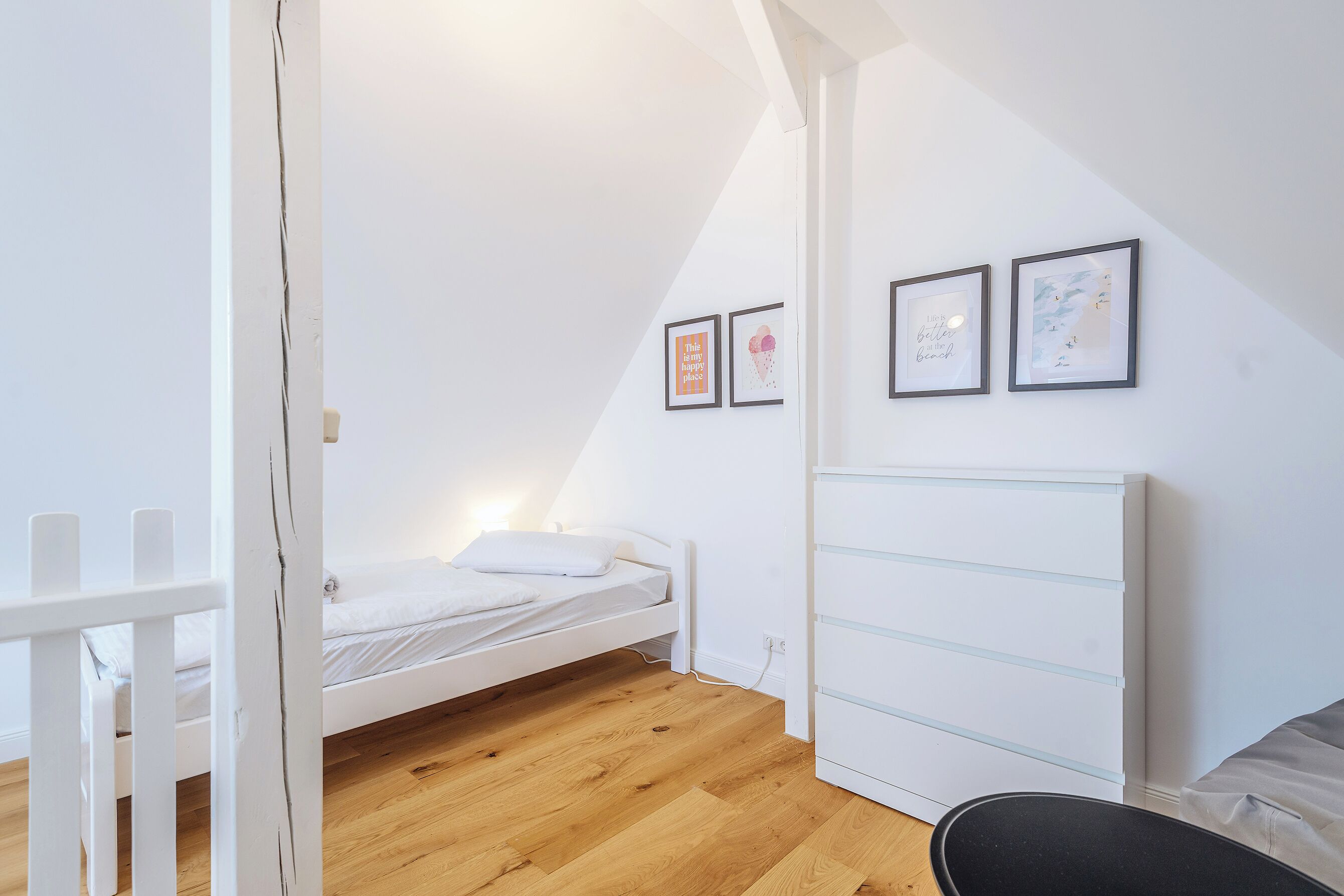 Een slaapkamer met een wit bed, een witte ladekast en een witte inloopkast. Er hangen twee afbeeldingen in lijsten aan de muur.