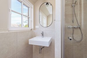 A bathroom with a white sink, a mirror, and a shower. - Contemporary comfort under thatch - your maisonette on the Bodden (Born a. Darß)