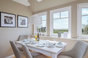 A dining area with a white table set for four, framed pictures on the wall, and large windows with a view. - Contemporary comfort under thatch - your maisonette on the Bodden (Born a. Darß)
