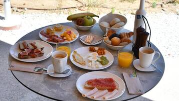 Una mesa redonda con alimentos para el desayuno, una silla y una lámpara de mesa.