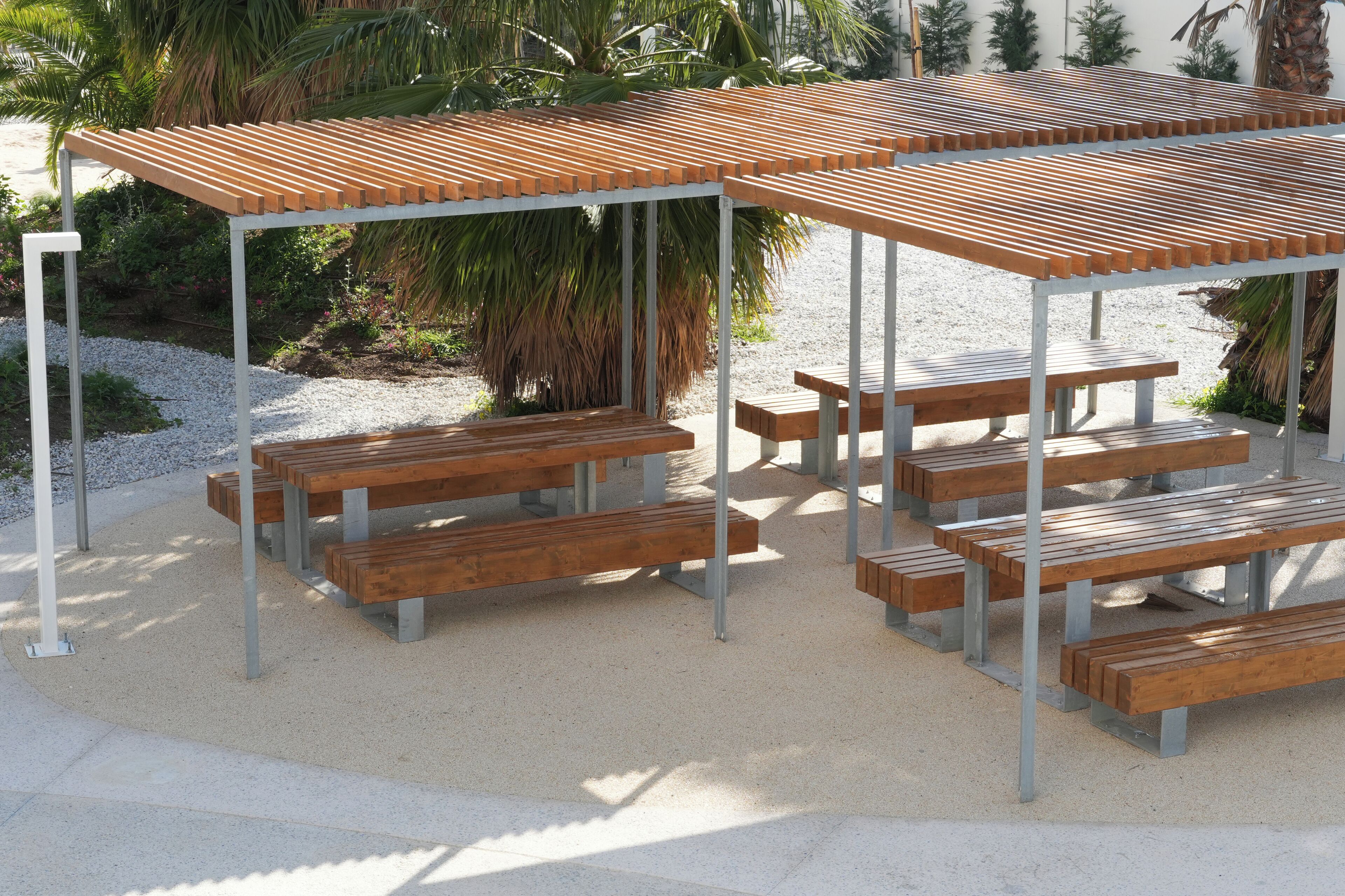 Un espace extérieur abrité, doté de plusieurs bancs en bois et d’une structure en métal.