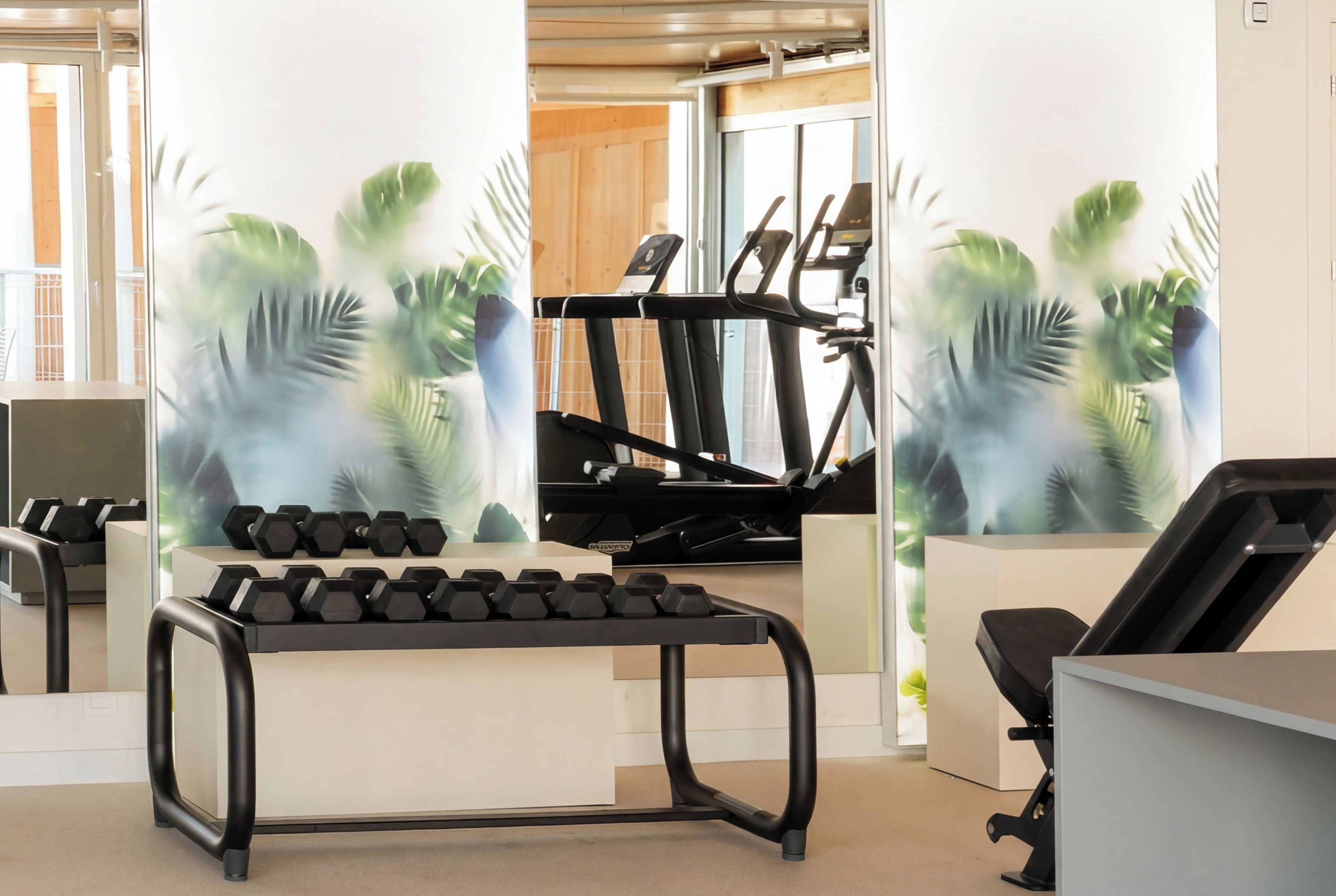 A gym with exercise equipment, including treadmills and dumbbells, and a wall with a tropical plant mural.