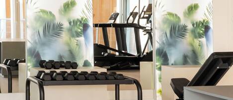 A gym with exercise equipment, including treadmills and dumbbells, and a wall with a tropical plant mural.