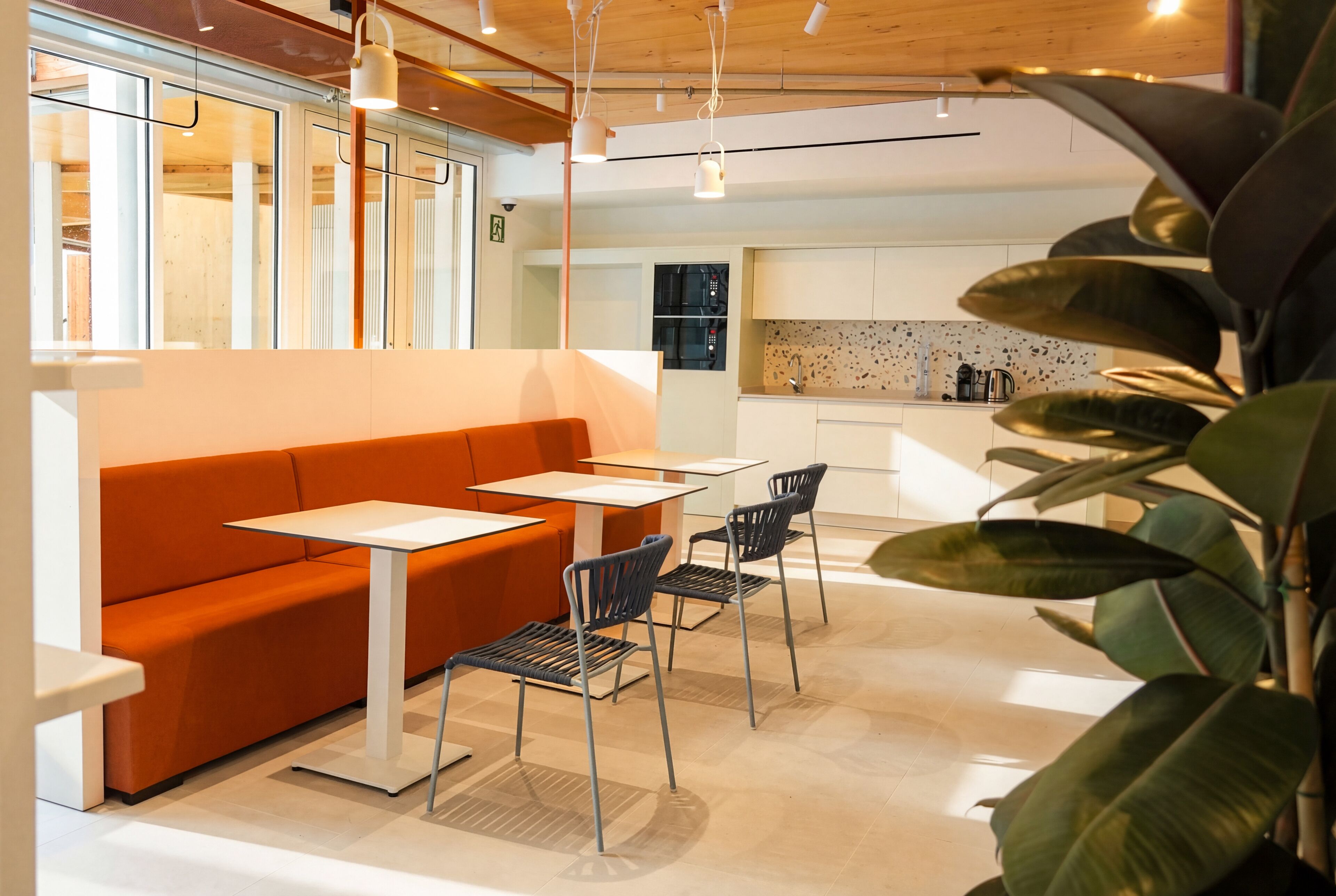 A modern interior with a sofa, tables, chairs, and a kitchen area.