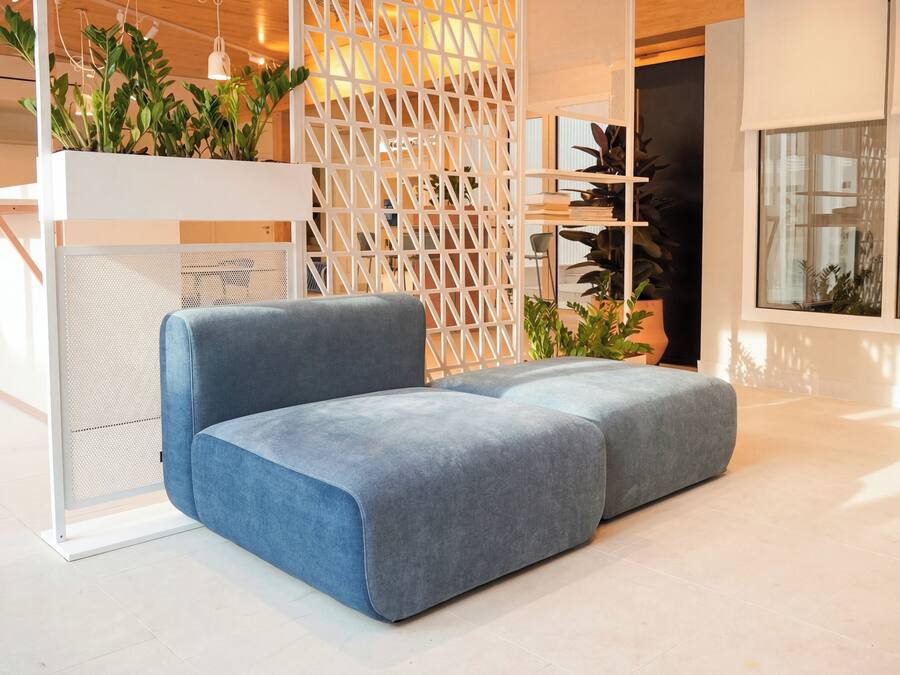 Un interior moderno con un sofá azul, separadores blancos y plantas en macetas.