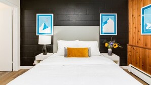 Een hotelkamer met een groot bed, witte beddengoed, een mosterdgeel kussen, twee nachtkastjes met lampen en een houten paneelwand.