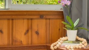 Een hoek van een kamer met houten lambrisering, een raam met uitzicht op groen, een potplant en een ketting van houten kralen.