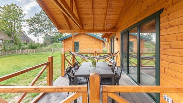 A wooden deck with a table and chairs, a hammock, and a view of a house in the background. - Vacation home "Huus Klee" in Kating for up to 4 people (Kating)