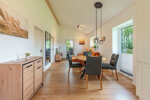 A modern kitchen with wooden cabinets, a dining area with a round table and chairs, and a view of greenery outside. - "Huus Schoop" Vacation Home in Kating for up to 4 people (Kating)
