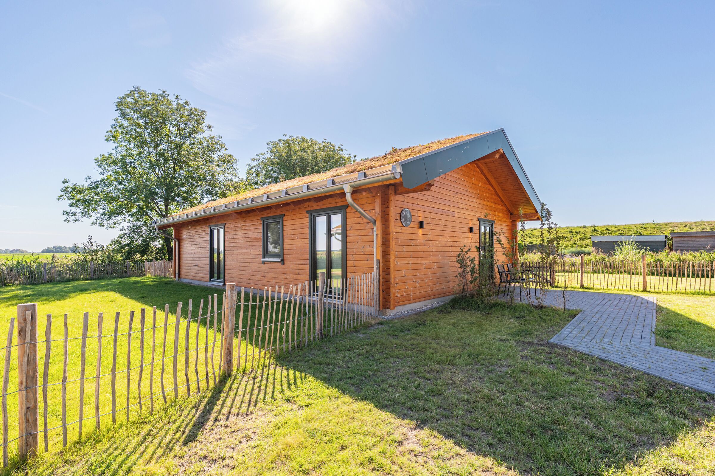 A wooden cabin with a sloped roof, a fenced yard, and a clear sky.