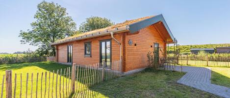 A wooden cabin with a sloped roof, a fenced yard, and a clear sky.