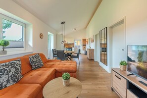 A modern living room with a sectional sofa, a round coffee table, and a television on a wooden cabinet. - "Huus Schoop" Vacation Home in Kating for up to 4 people (Kating)